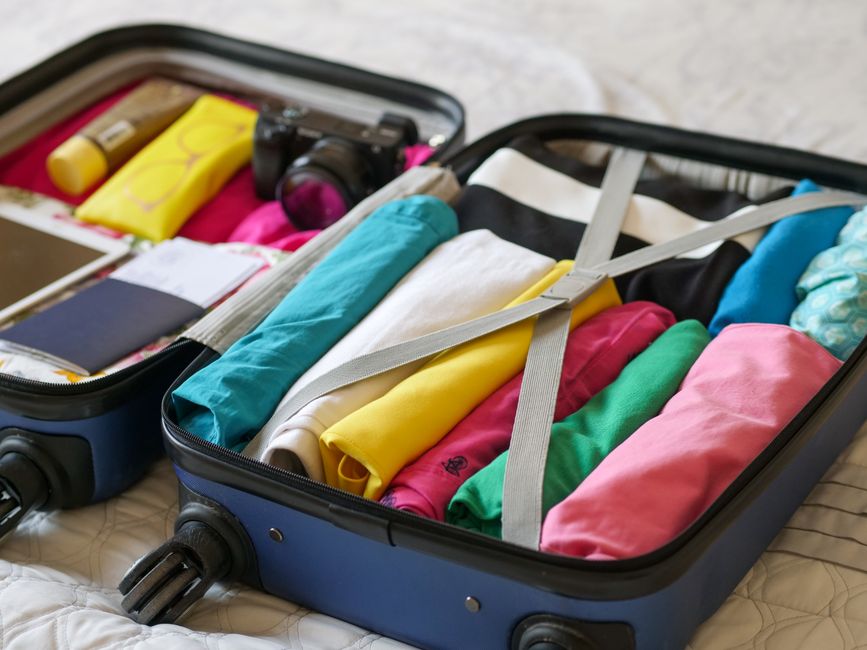 A neatly folded, travel-ready trench coat inside an open suitcase alongside other capsule wardrobe items.
