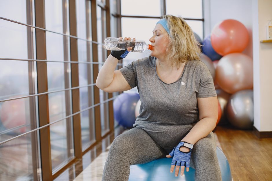 A person stands by a large window, stretching gently while holding a glass of water, capturing the importance of hydration and daylight exposure for adjusting to new time zones.