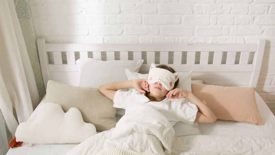 A soft, plush eye mask and a pair of discreet earplugs rest on a pristine white hotel bed, symbolizing essential tools for creating a peaceful sleep environment while traveling.
