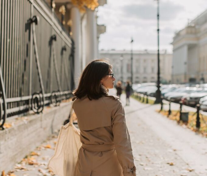 A professional woman in a classic beige trench coat walking purposefully on a rainy city street with an umbrella.
